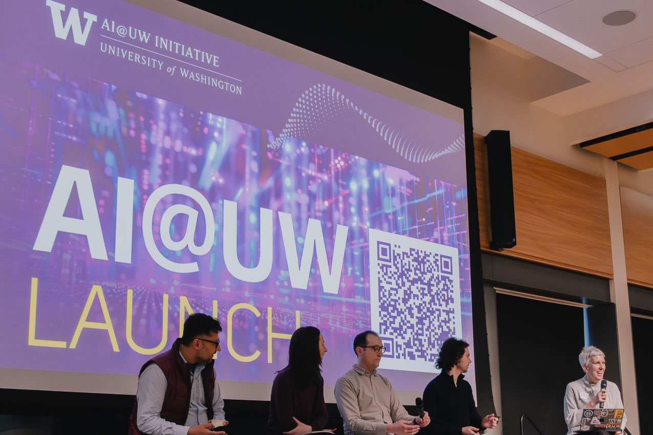 Four speakers and a moderator sit on stage at an event