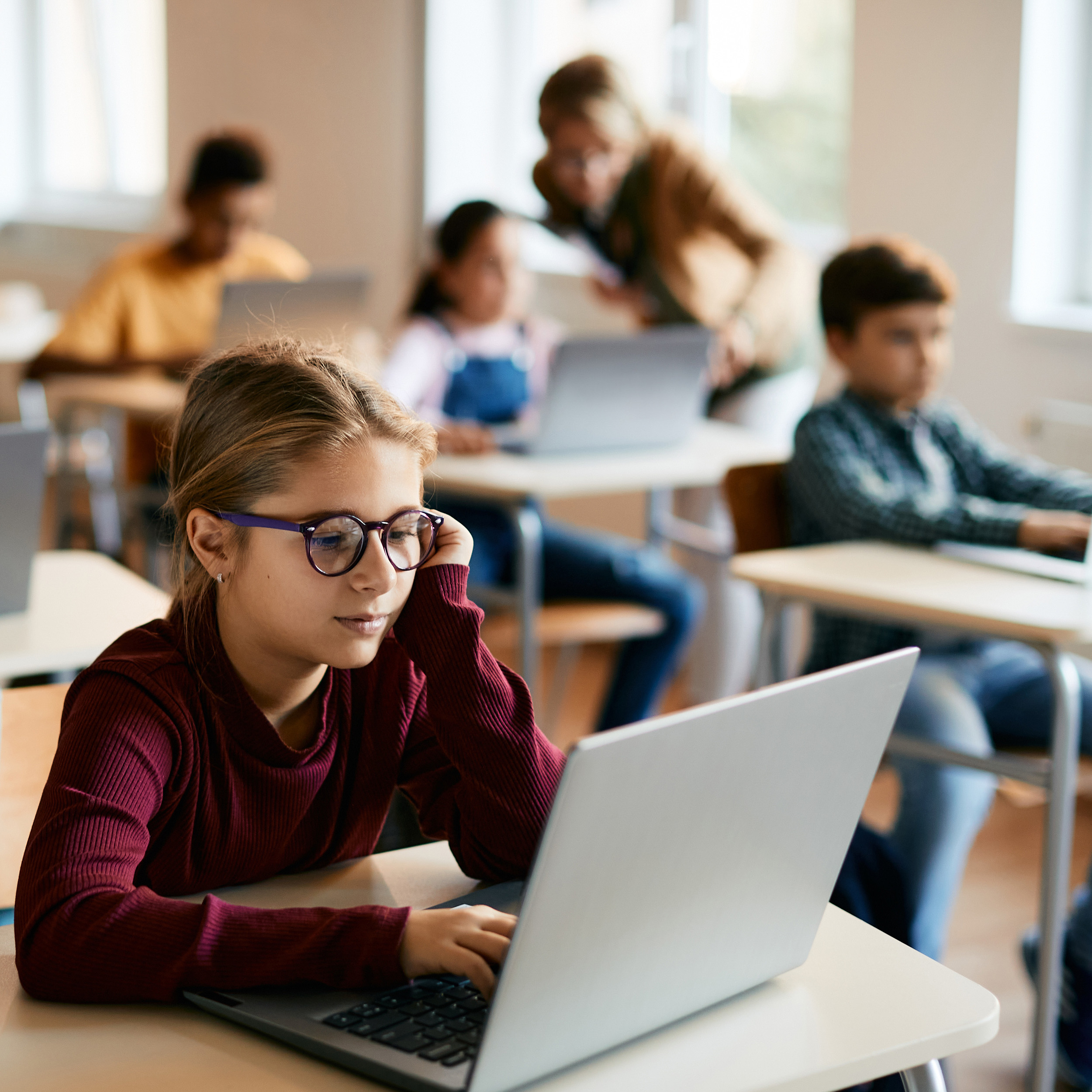 A girl with glasses works on a computer while seated in an elementary school classroom
